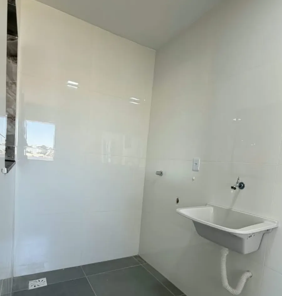Área de serviço com tanque, paredes de azulejo branco e piso cinza