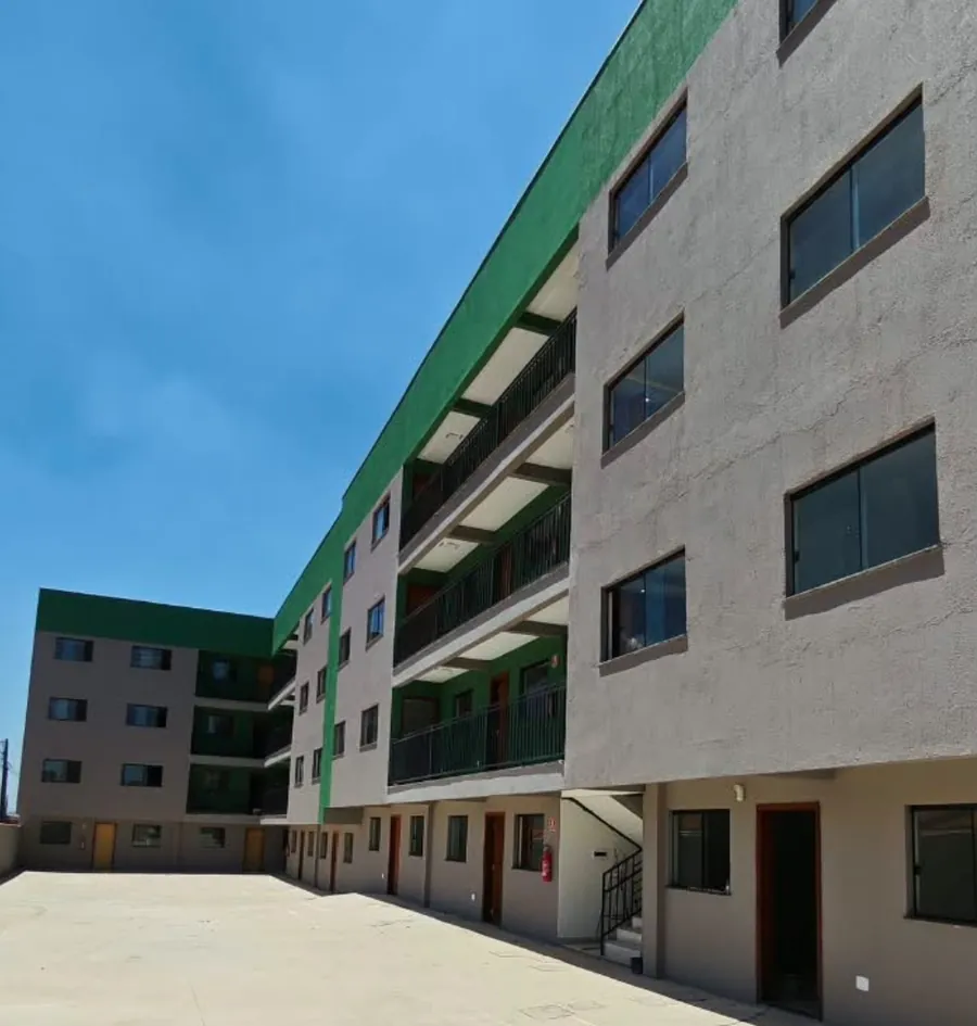 Prédio do residencial visto do pátio, com acabamento cinza e detalhes verdes, sob céu azul