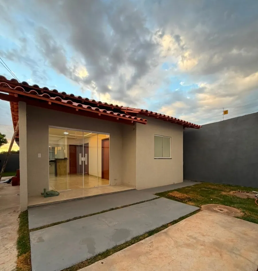 Fachada da casa, com telhado colonial, porta de vidro e jardim, ao pôr do sol